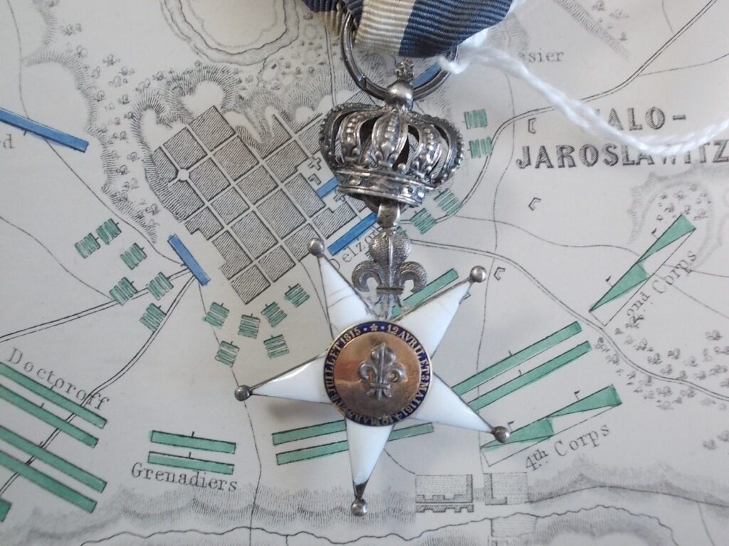 Decorazione del Giglio: stella a sei punte smaltata di bianco con giglio fra le punte e corona reale in argento; nastro bianco listato d'azzurro.