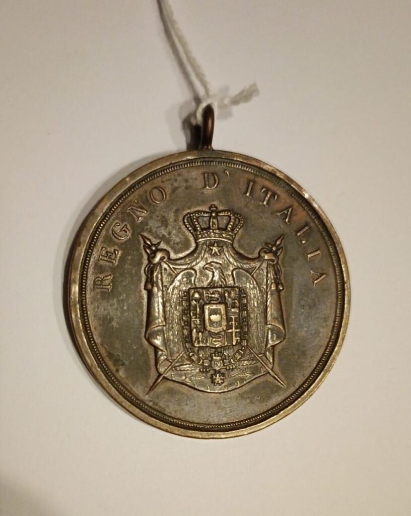 Medaglia del Regno d'Italia: al dritto lo stemma coronato con le armi imperiali e la legenda «REGNO D'ITALIA».
