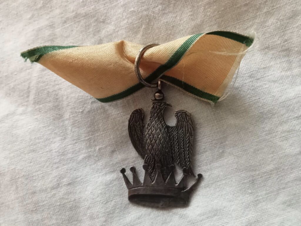 Insegna da cavaliere dell'Ordine della Corona di Ferro: aquila imperiale sulla corona ferrea, nastro verde bordato d'arancio.